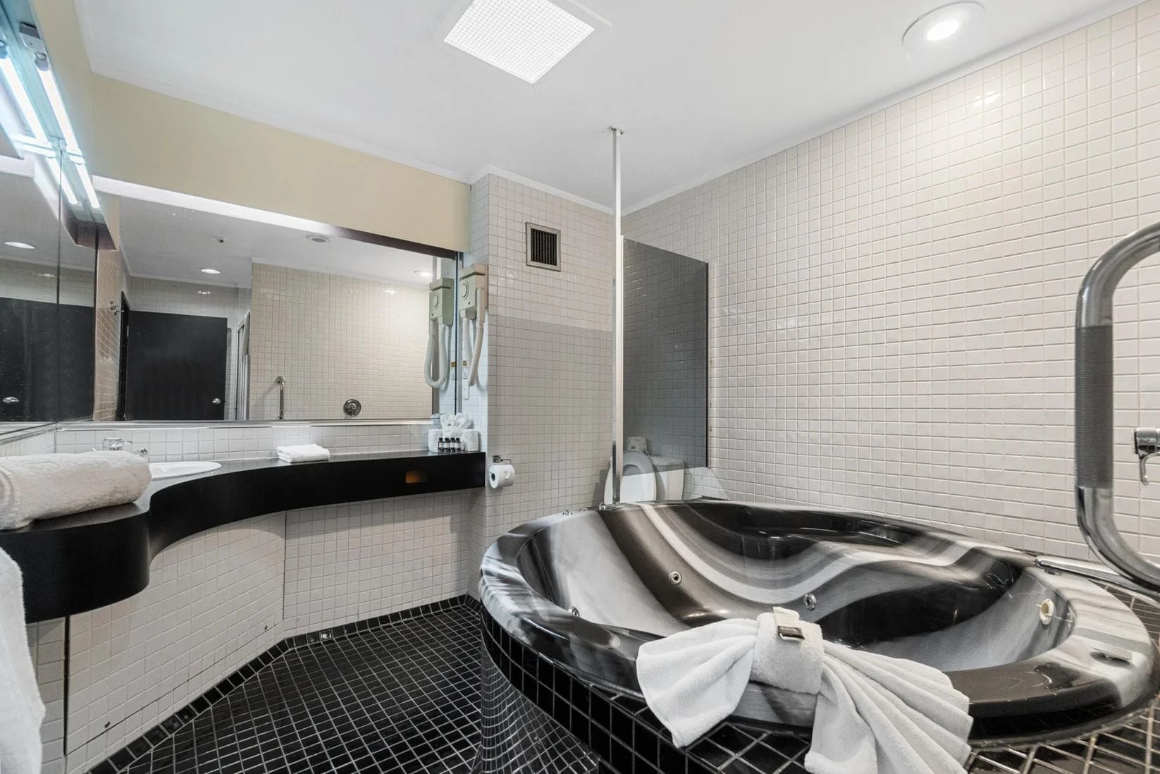A modern bathroom with a black and white color scheme, featuring a large bathtub, a vanity with a mirror, and a shower area.
