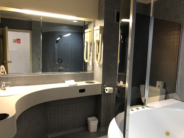 A modern bathroom with a large mirror, a bathtub, a shower, and a toilet. - Alcamo Hotel & Conference Centre (Hamilton)