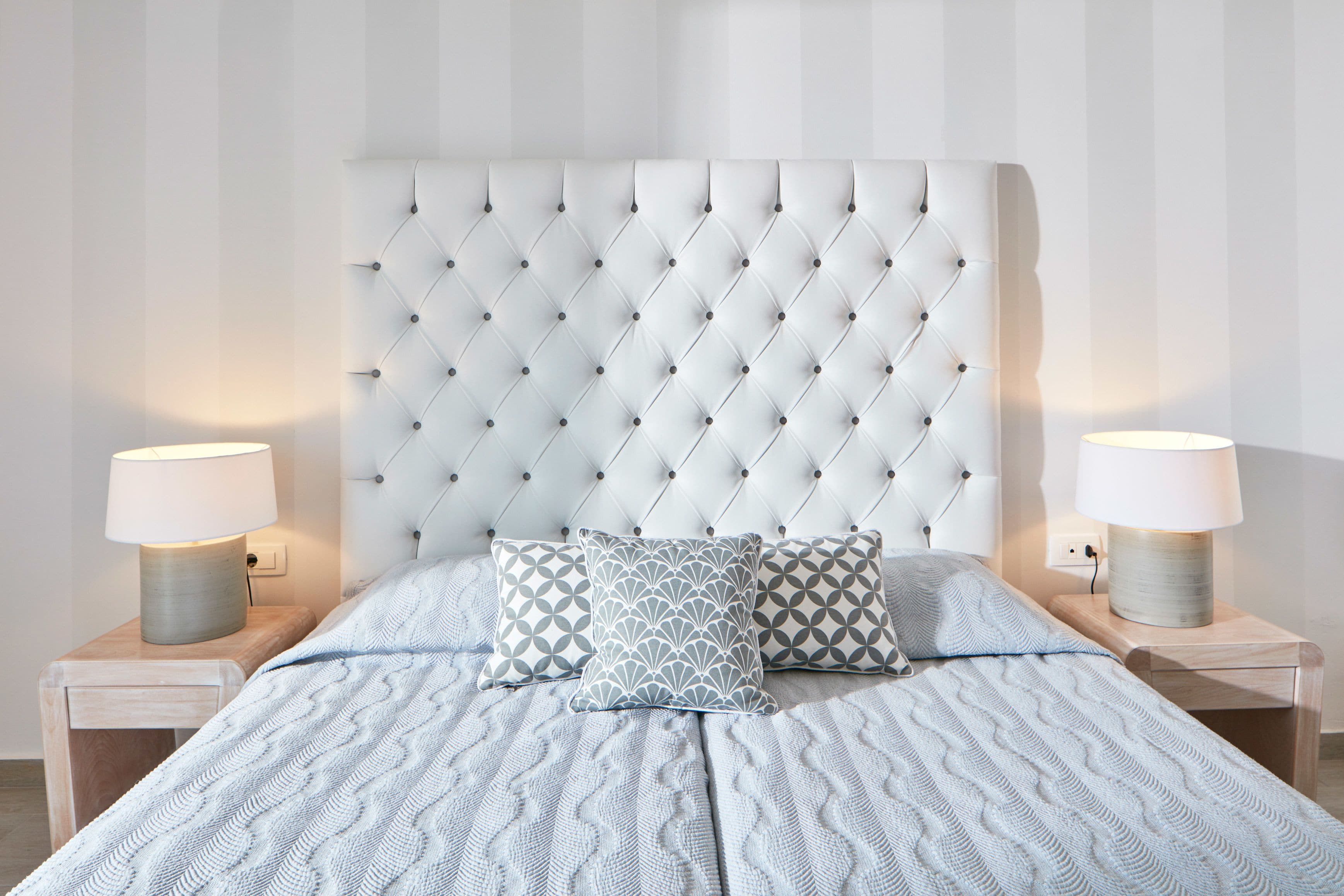 A neatly made bed with a tufted headboard, two bedside lamps, and patterned pillows.