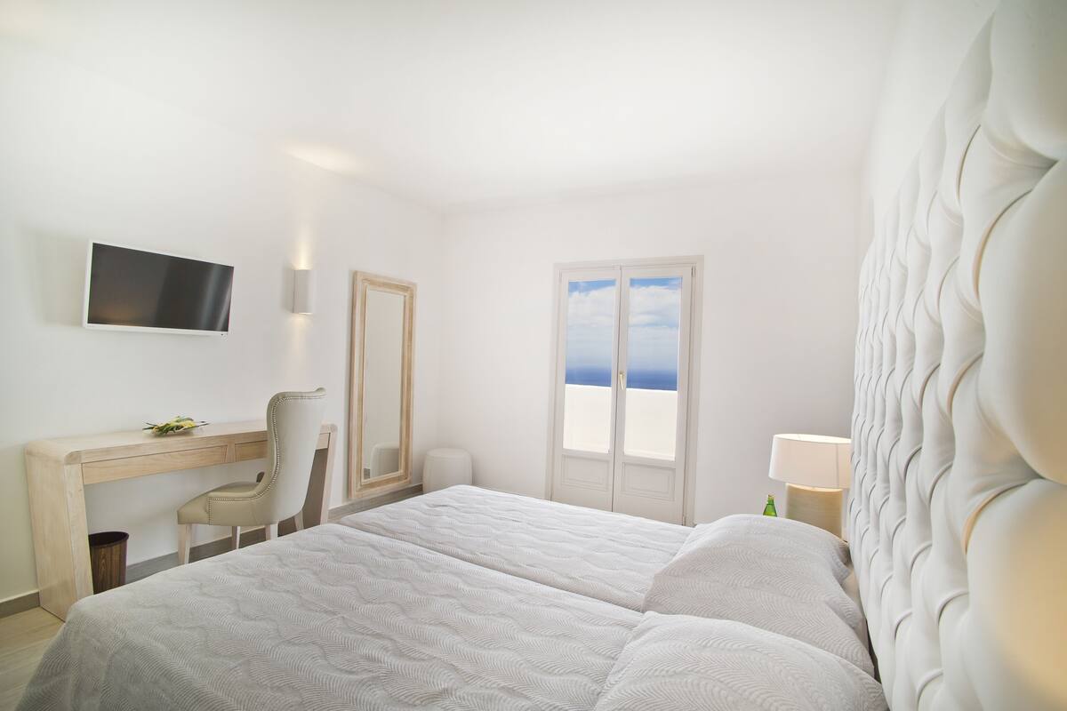 Un dormitorio con cama, escritorio, silla, televisor y ventana con vistas.
