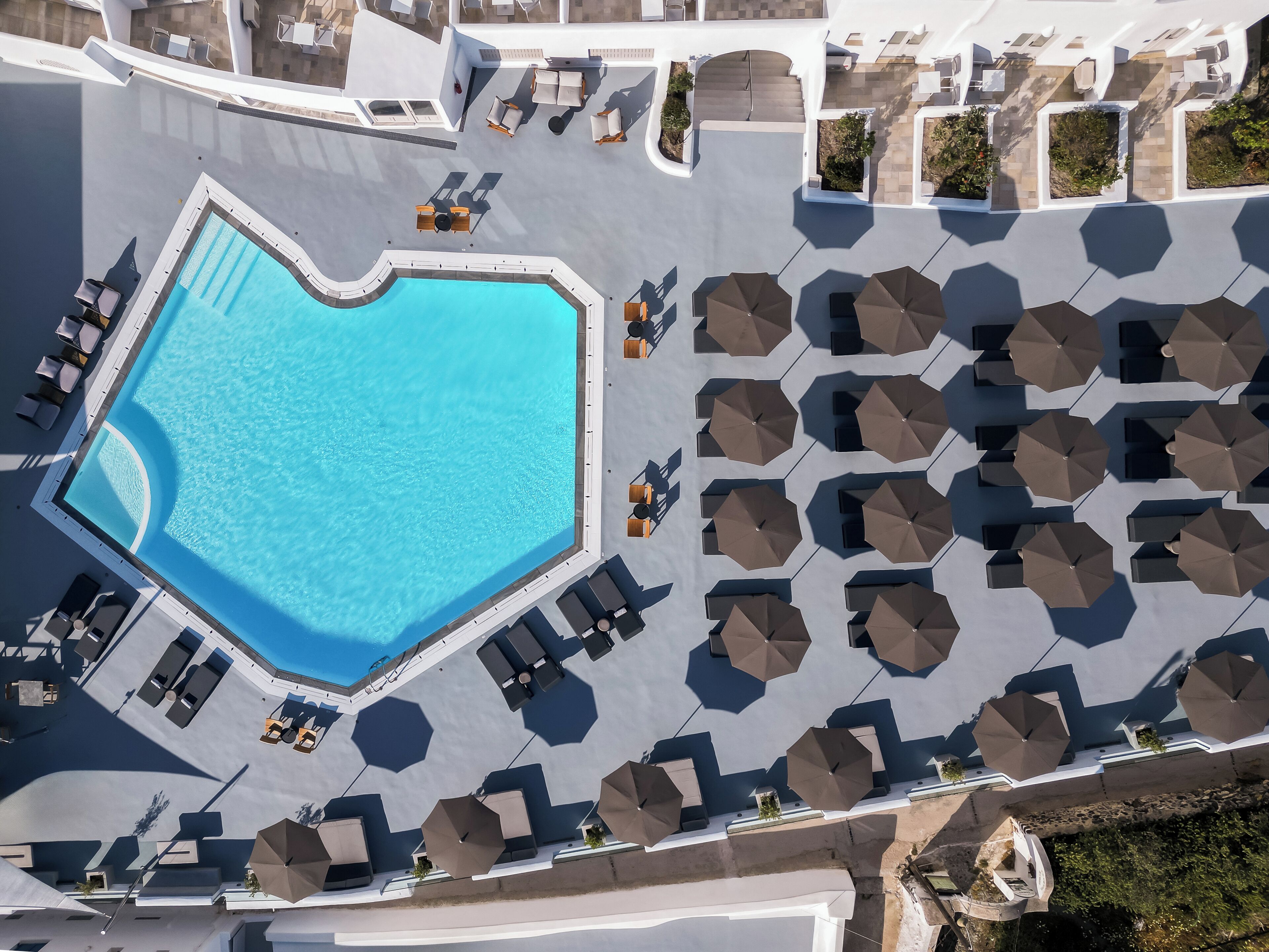 Vue aérienne d’un hôtel doté d’une grande piscine en forme de cœur, entourée de transats et de parasols.