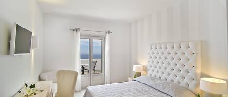 A hotel room with a large bed, a chair, a table, and a view of the sea through a door.