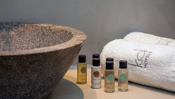 Uma bacia de pedra, três frascos de produtos de cuidados corporais Geneva Gulf e uma toalha branca com a inscrição 'Geneva Gulf'.