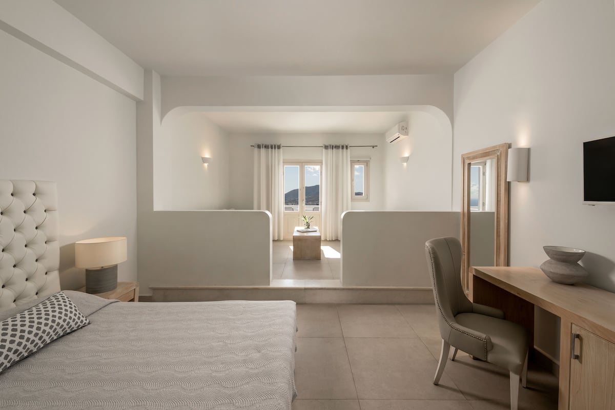 Habitación de hotel moderna con una cama grande, un escritorio, una silla y vistas a un baño y un balcón.