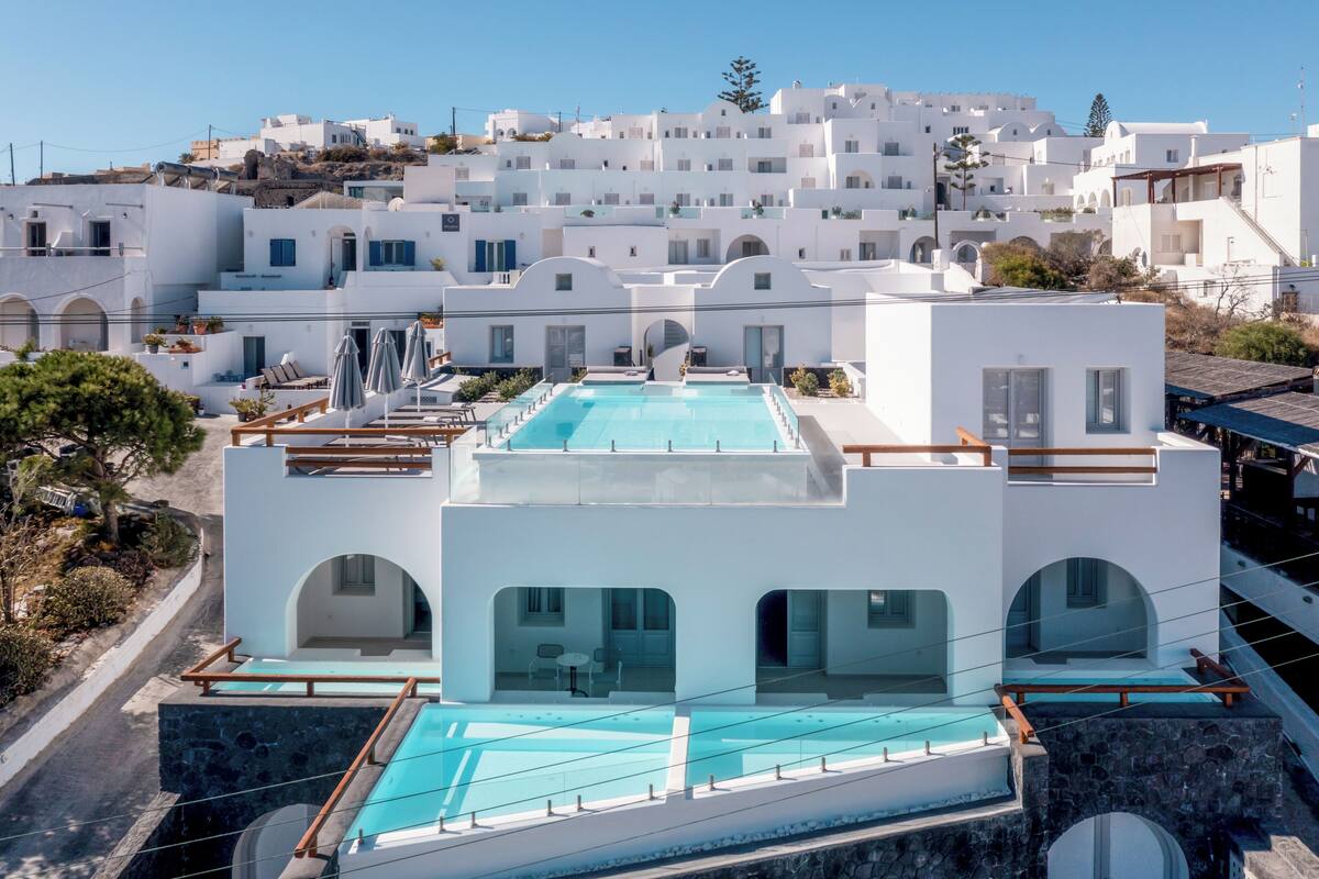 Un hotel moderno con piscina en la azotea, arquitectura blanca y vistas del pueblo circundante.