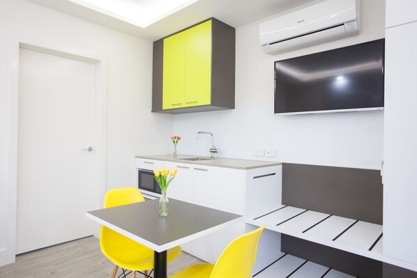 A compact kitchen with a dining area, a built-in oven, and a flat-screen TV mounted above the counter. - Abode St Kilda (St Kilda)