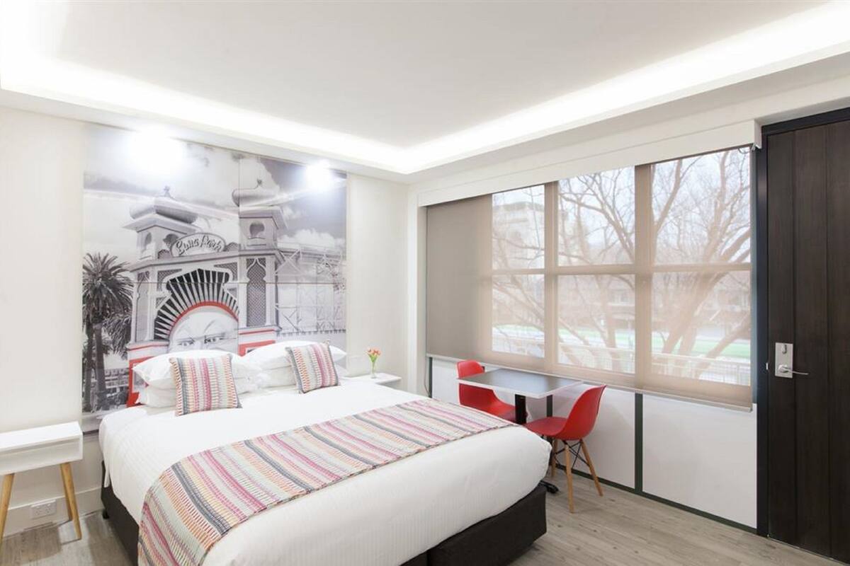 Un dormitorio moderno con una cama grande, un escritorio y un ventanal con vistas a árboles.