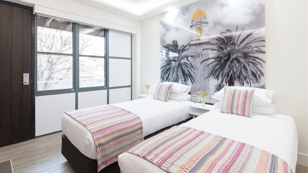 A hotel room with two beds, a large window, and a mural of palm trees and a building.