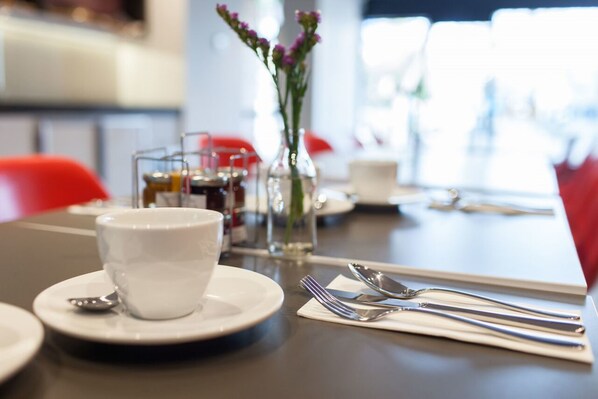 A dining table with a white cup and saucer, a glass vase with flowers, and neatly arranged cutlery.