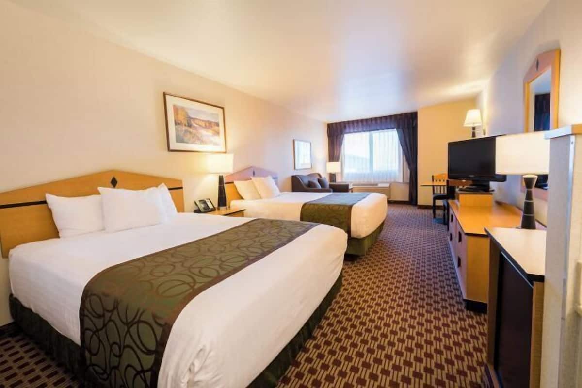 A hotel room with two beds, a desk, a television, and a window with curtains.