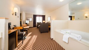 A hotel room with a desk, chairs, a sofa, a large mirror, and a bathtub with towels. - Crystal Inn Hotel & Suites Great Falls (Great Falls)