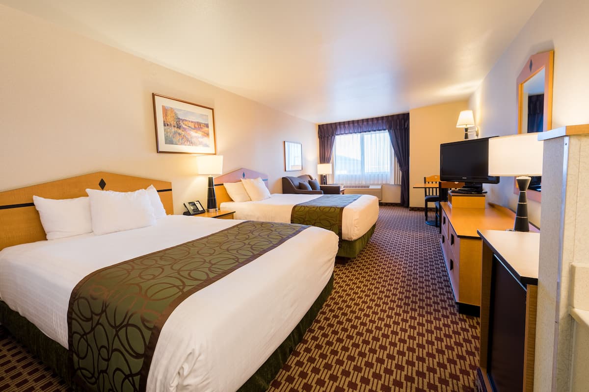 A hotel room with two beds, a desk, a TV, and a window with curtains.