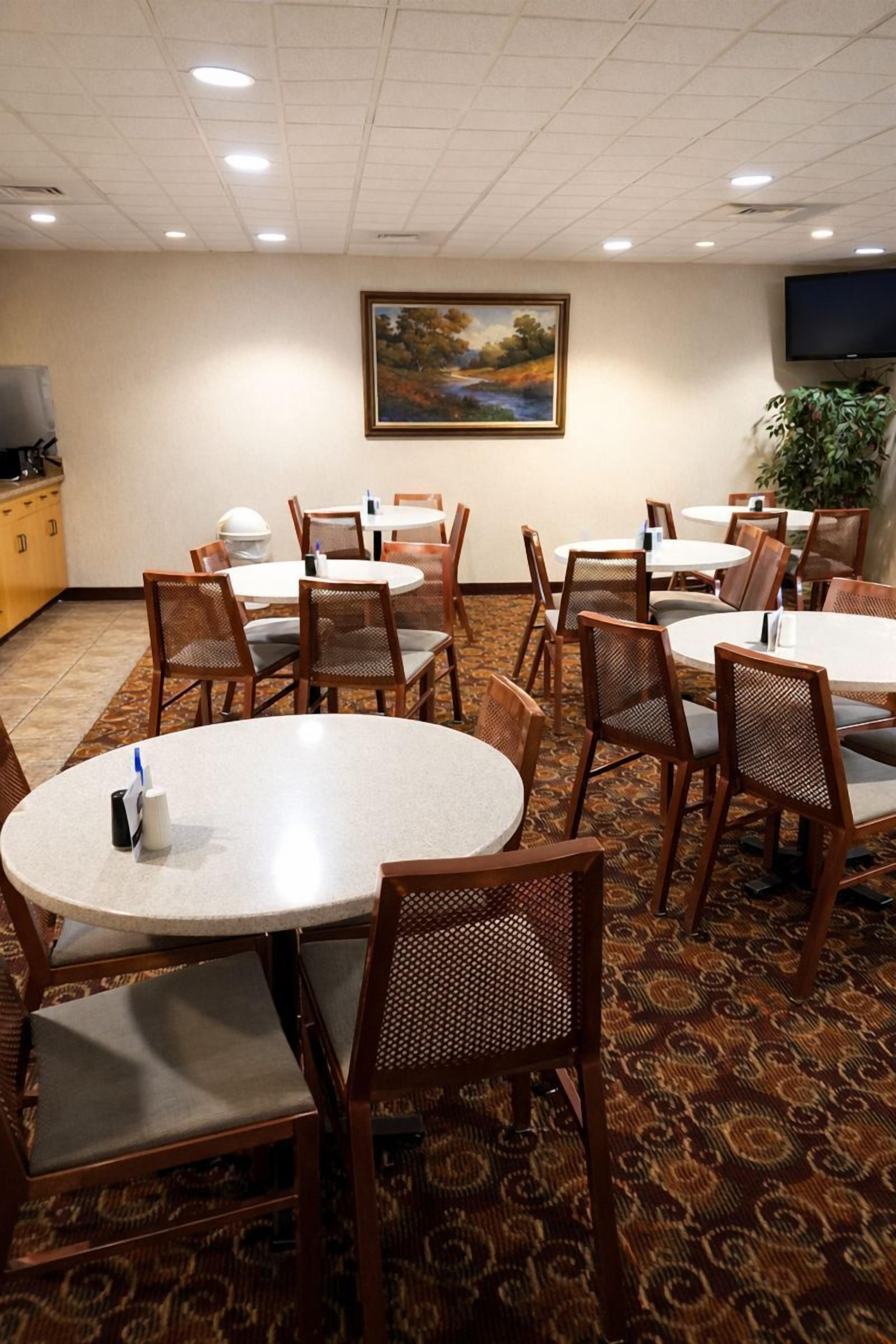 A conference room with round tables and chairs, a painting on the wall, and a television on the ceiling.