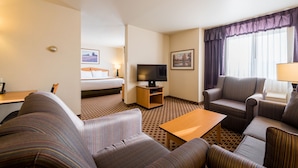 A hotel room with a bed, a TV, a sofa, a coffee table, and a window with curtains. - Crystal Inn Hotel & Suites Great Falls (Great Falls)