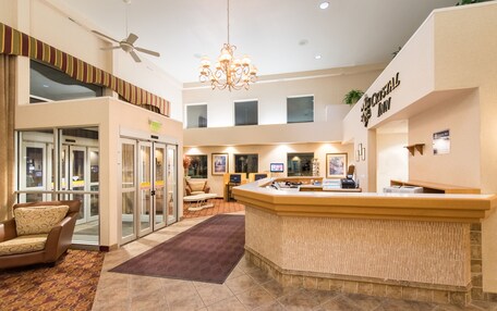 A hotel lobby with a reception desk, seating area, and glass doors leading to rooms.