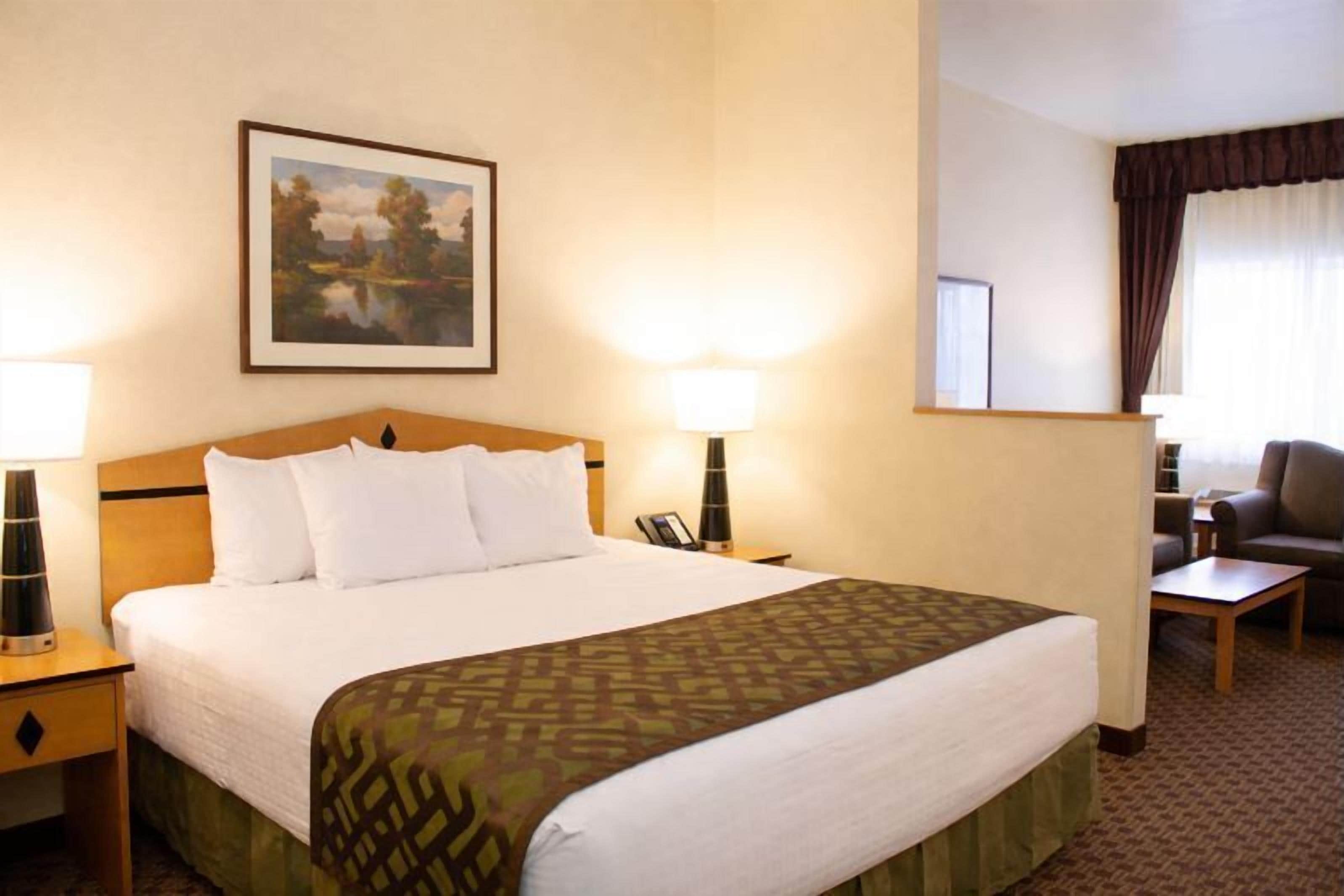 A hotel room with a large bed, two bedside lamps, a desk, a chair, and a painting on the wall.