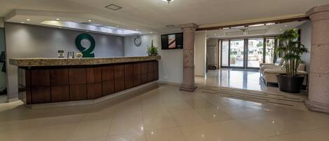 A hotel reception area with a wooden reception desk, a large number '2' sign, a clock, and a television screen.