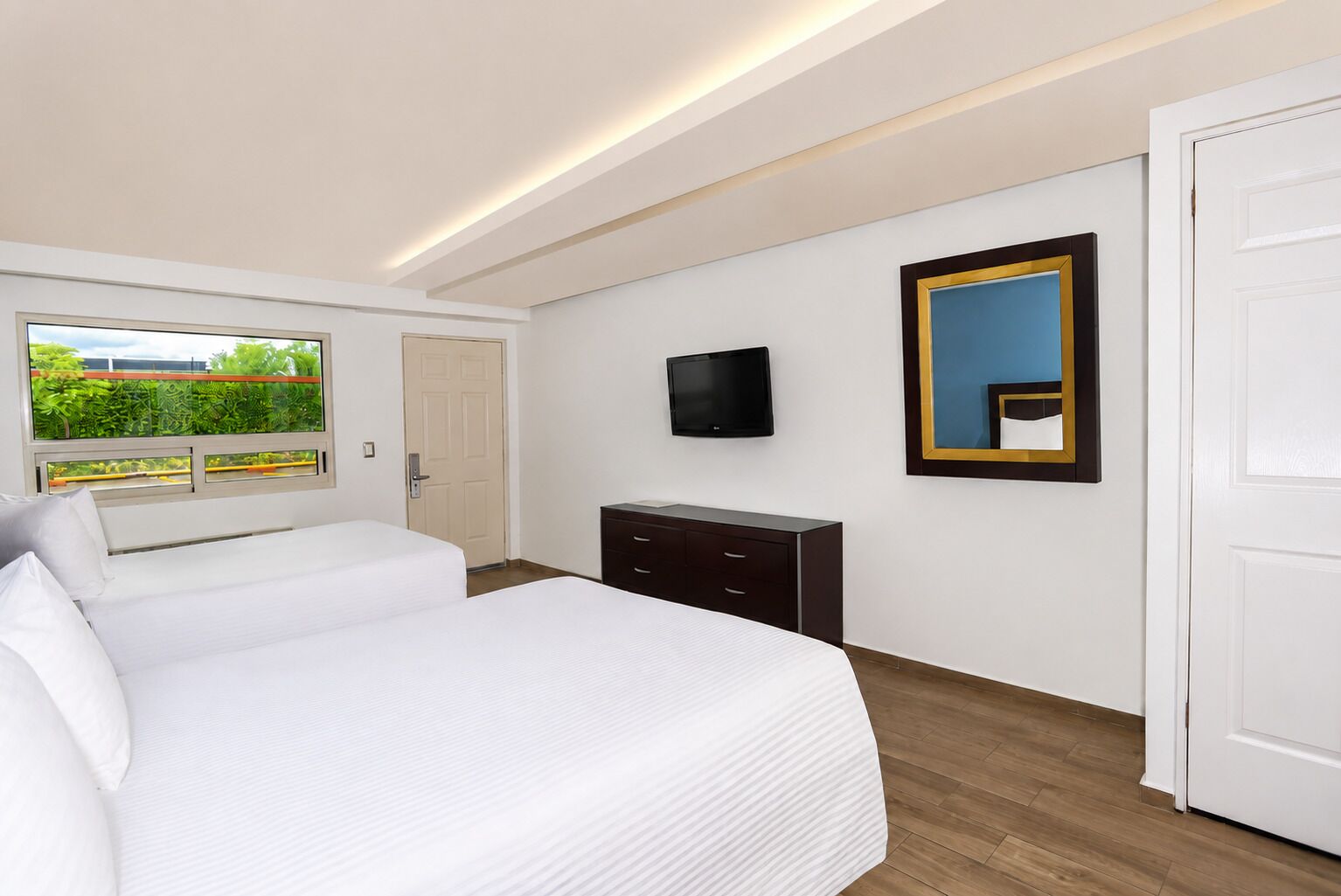 Habitación de hotel con dos camas, televisión, cómoda y ventana con vistas a zonas verdes.