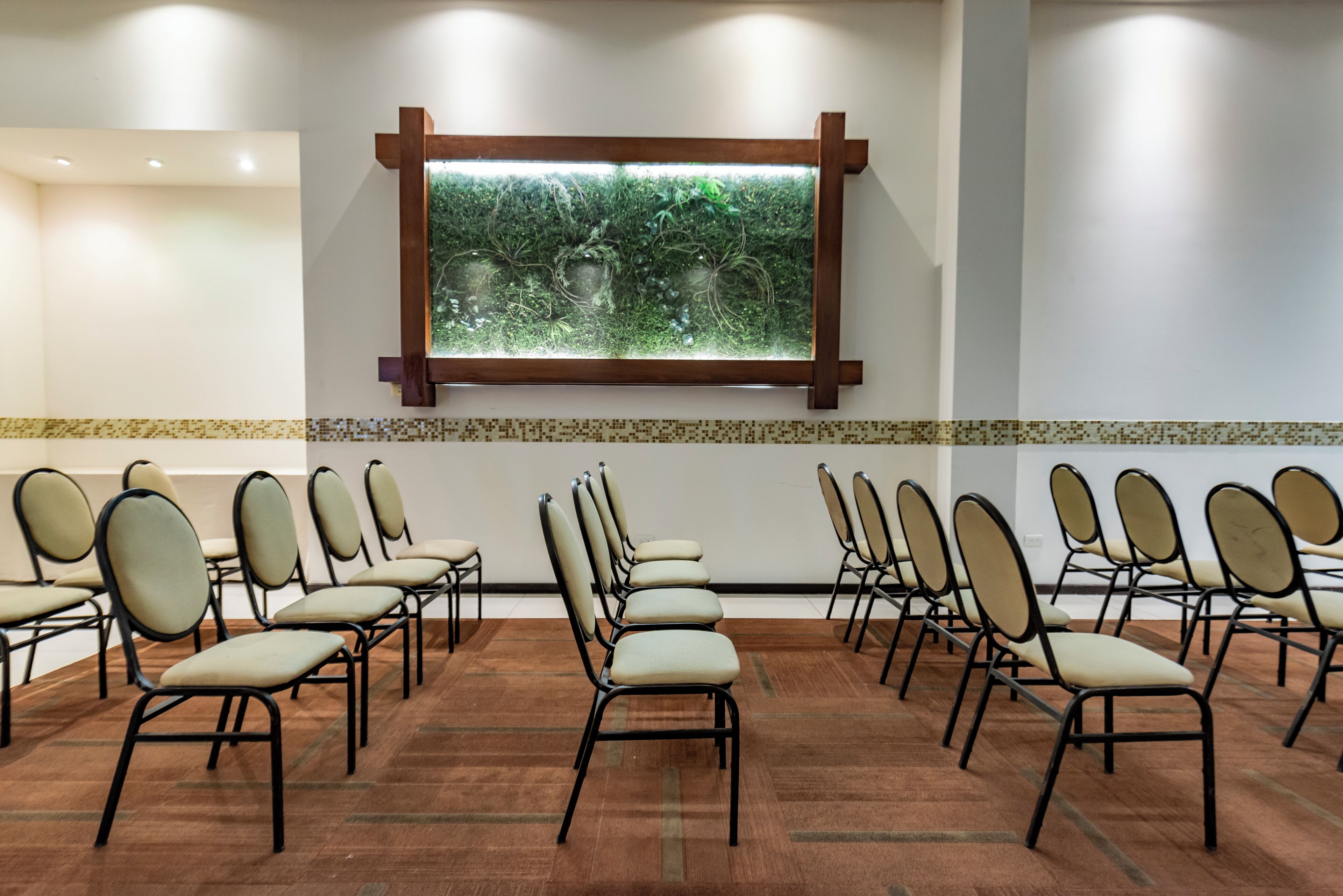 A conference room with rows of chairs, a large window with a view of greenery, and a wooden cross on the wall.