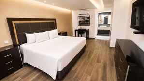 A modern hotel room with a large bed, a desk, a TV, and a bathroom visible through an open door. - Quinta Dorada Hotel and Suites (Saltillo)