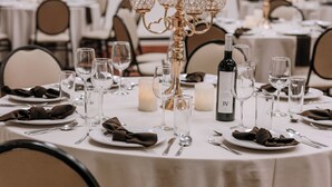 A banquet table set with plates, cutlery, glasses, and a bottle of wine, surrounded by chairs and a decorative candelabra. - Quinta Dorada Hotel and Suites (Saltillo)