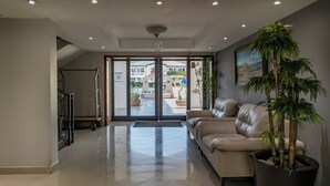 A spacious lobby with a leather sofa, a large potted plant, and a view of the outdoor area through glass doors. - Quinta Dorada Hotel and Suites (Saltillo)