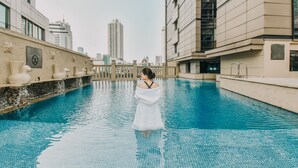 Zona de piscina con una persona de pie en el agua, rodeada de edificios modernos y un cielo despejado.
