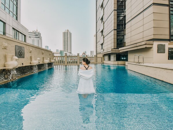 A pool area with a person standing in the water, surrounded by modern buildings and a clear sky. - JW Marriott Hotel Jakarta (Jakarta)