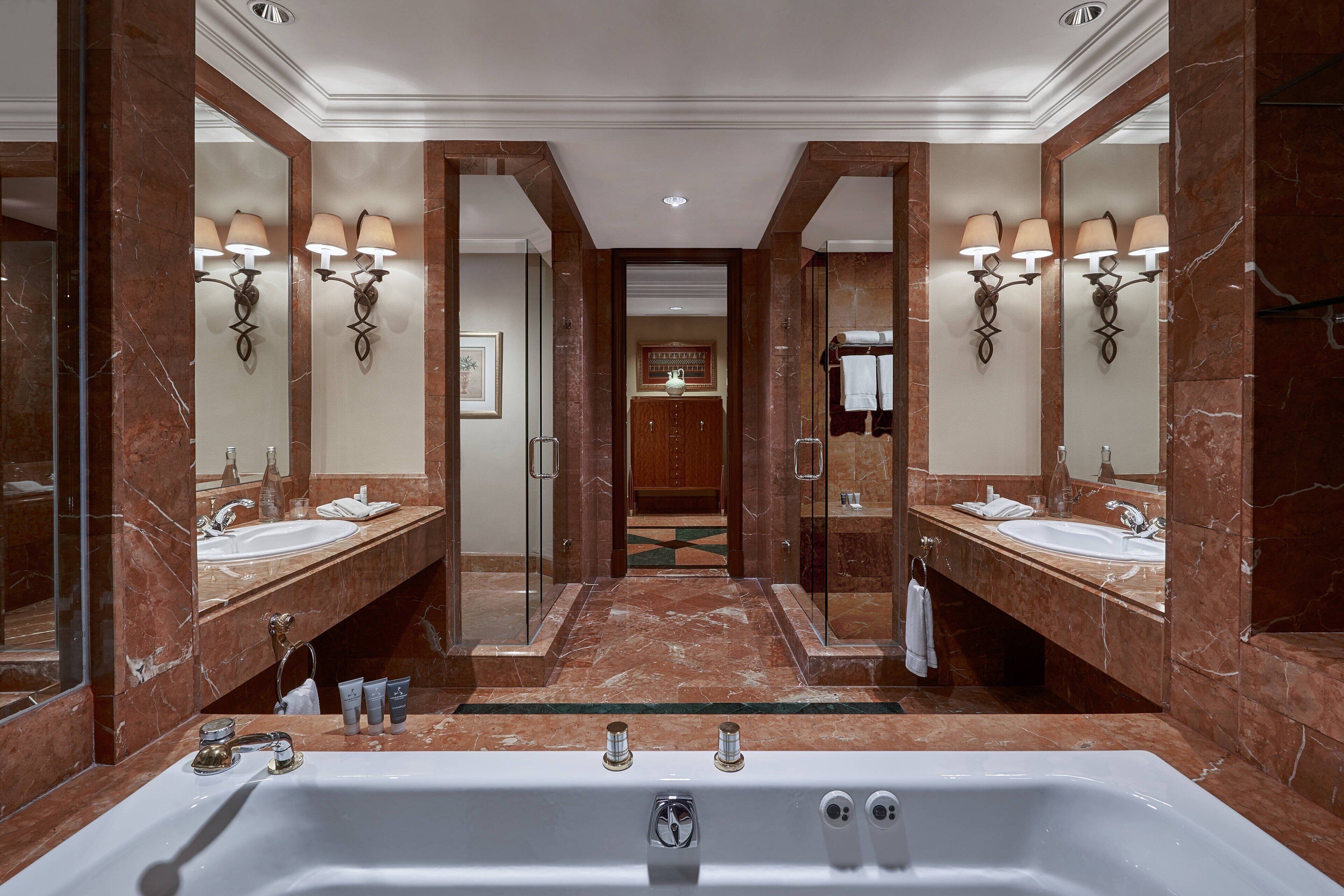 Un baño lujoso con dos lavamanos, una bañera grande y paredes de mármol.