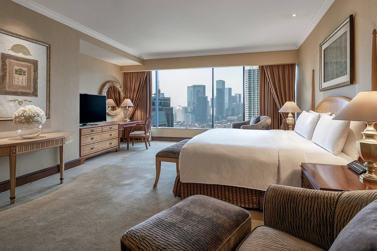Ein Hotelzimmer mit einem großen Bett, einem Schreibtisch, einem Fernseher und Blick auf die Stadtlandschaft.