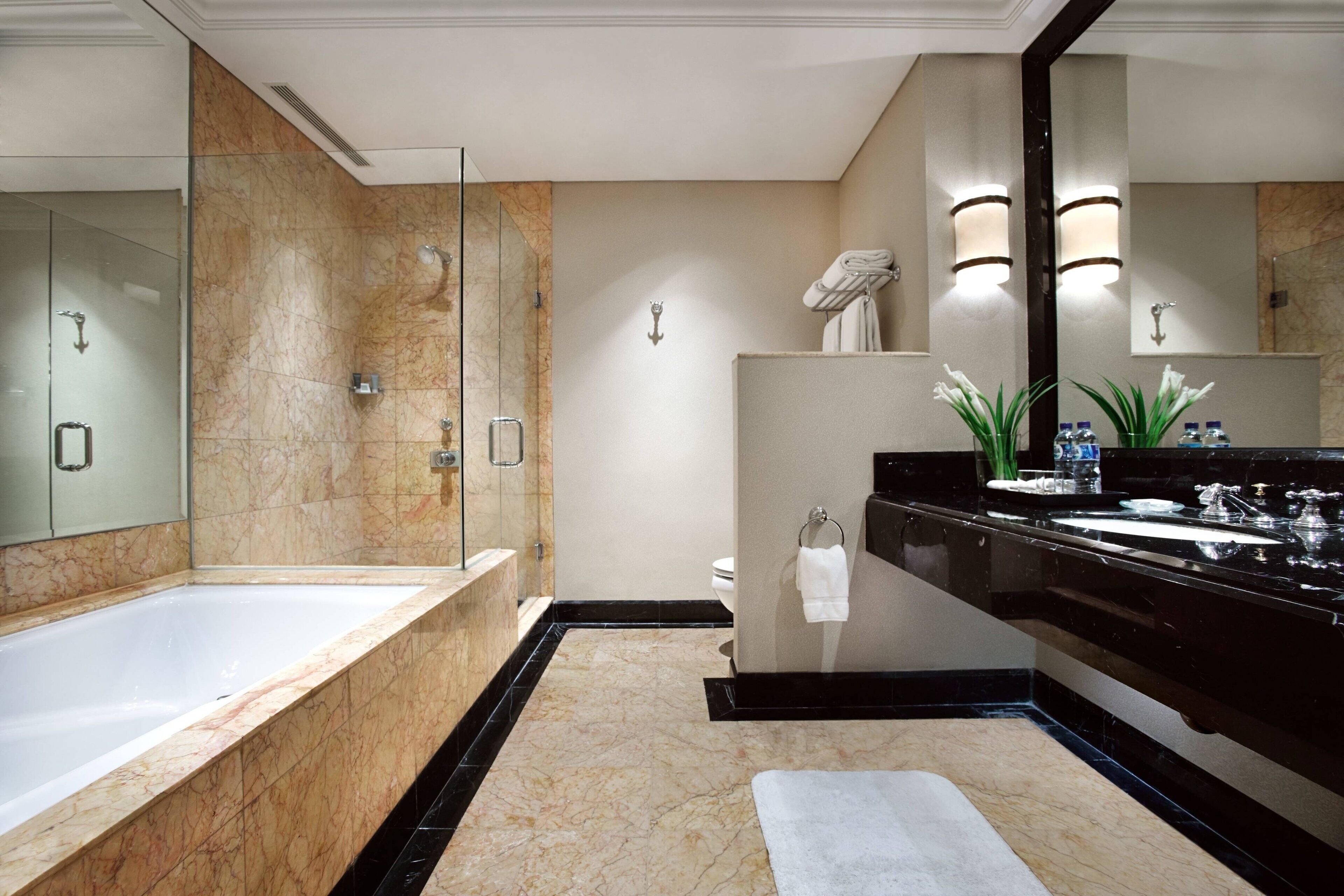 Une salle de bain moderne dotée d’une grande baignoire, d’une douche séparée, d’un meuble-lavabo avec un plan de travail noir et d’un grand miroir.