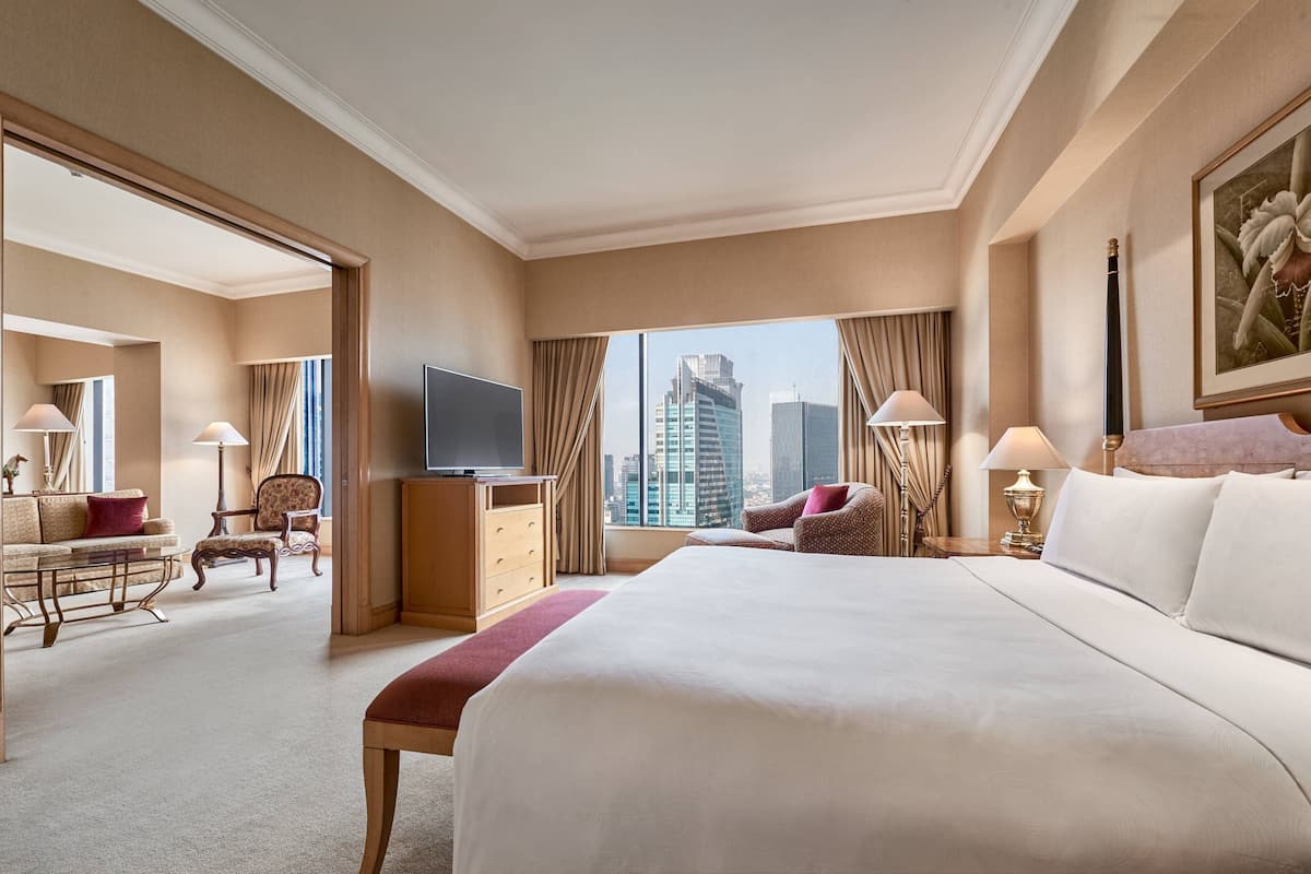 Ein Hotelzimmer mit einem großen Bett, einem Fernseher, einem Schreibtisch mit Lampe, einem Sessel und Blick auf die Stadt.
