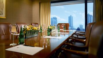 Un salón de conferencias con una larga mesa, sillas y vistas a un paisaje urbano a través de amplias ventanas.