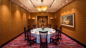 Une salle de conférence avec une table ronde, des chaises, un lustre et un tableau accroché au mur.