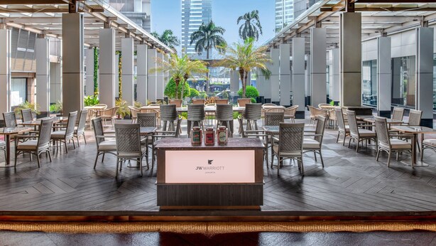Un restaurante JW Marriott con una barra central, rodeado de mesas y sillas para comer, y vistas a palmeras y edificios altos al fondo.
