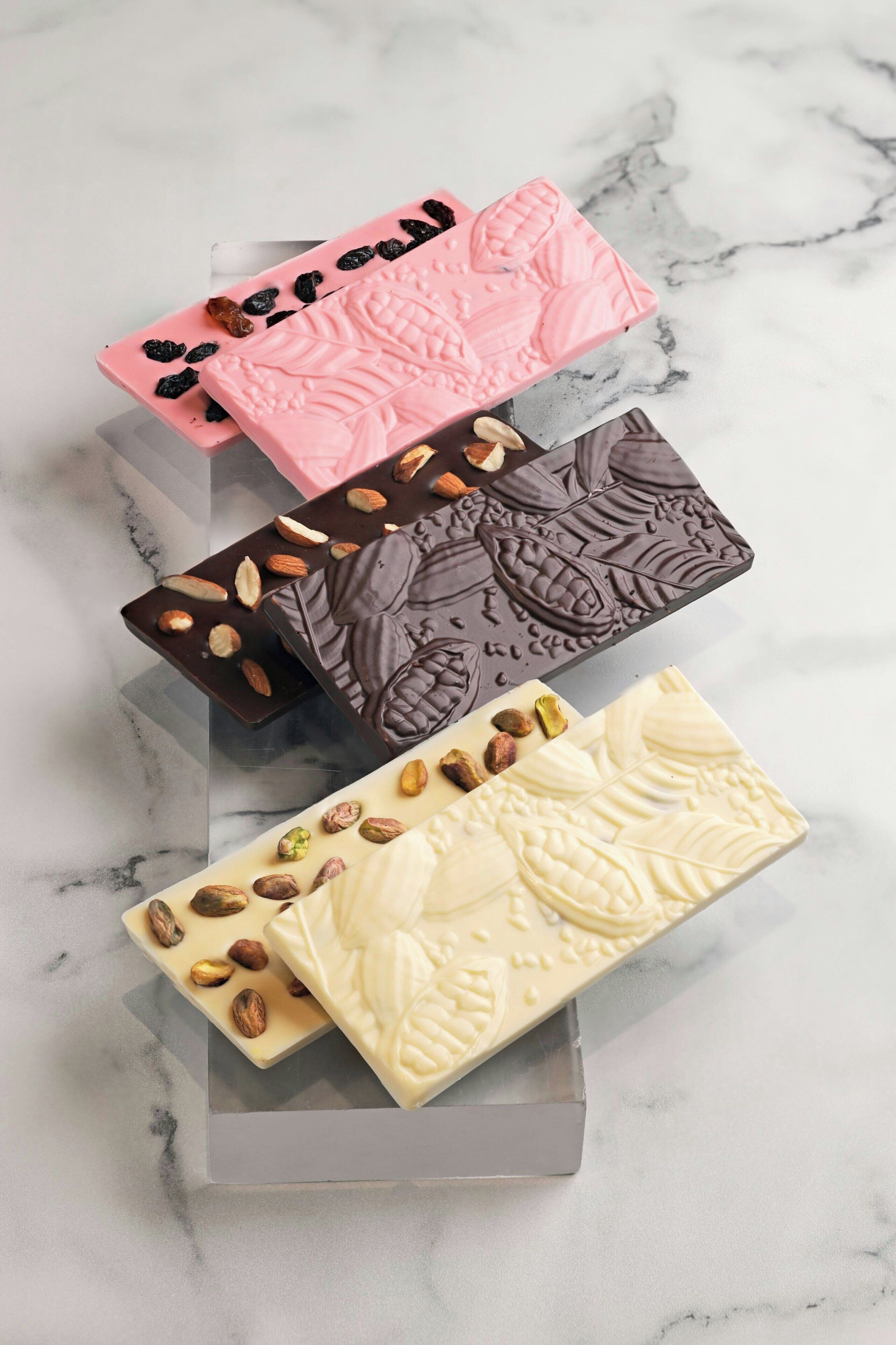 Four rectangular chocolate bars with different toppings on a marble surface.