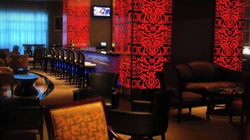 A dimly lit lounge area with patterned columns, a bar, and seating arrangements.