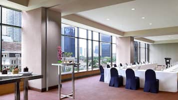 Un salón de conferencias con una larga mesa, sillas y vistas a edificios altos.