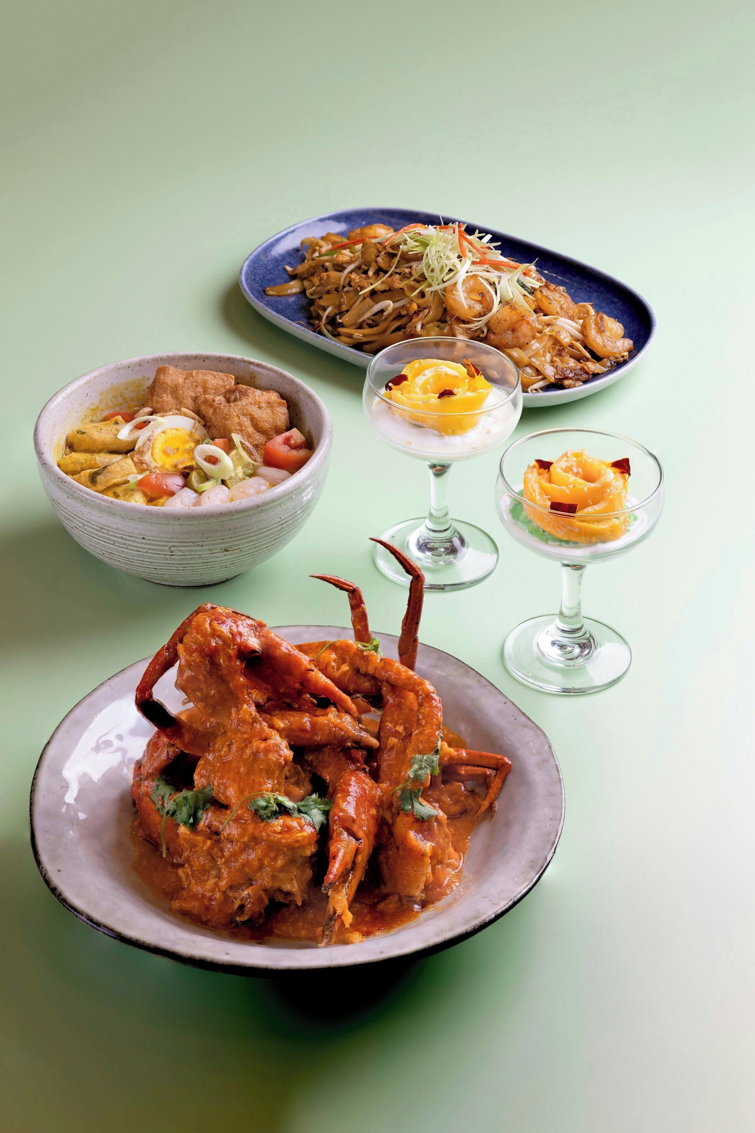 A variety of dishes including seafood, a bowl of soup, and desserts on a table.