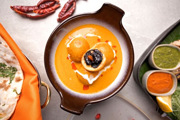 A bowl of soup with dumplings and a lemon wedge, accompanied by a plate of flatbread and two small bowls of sauce.