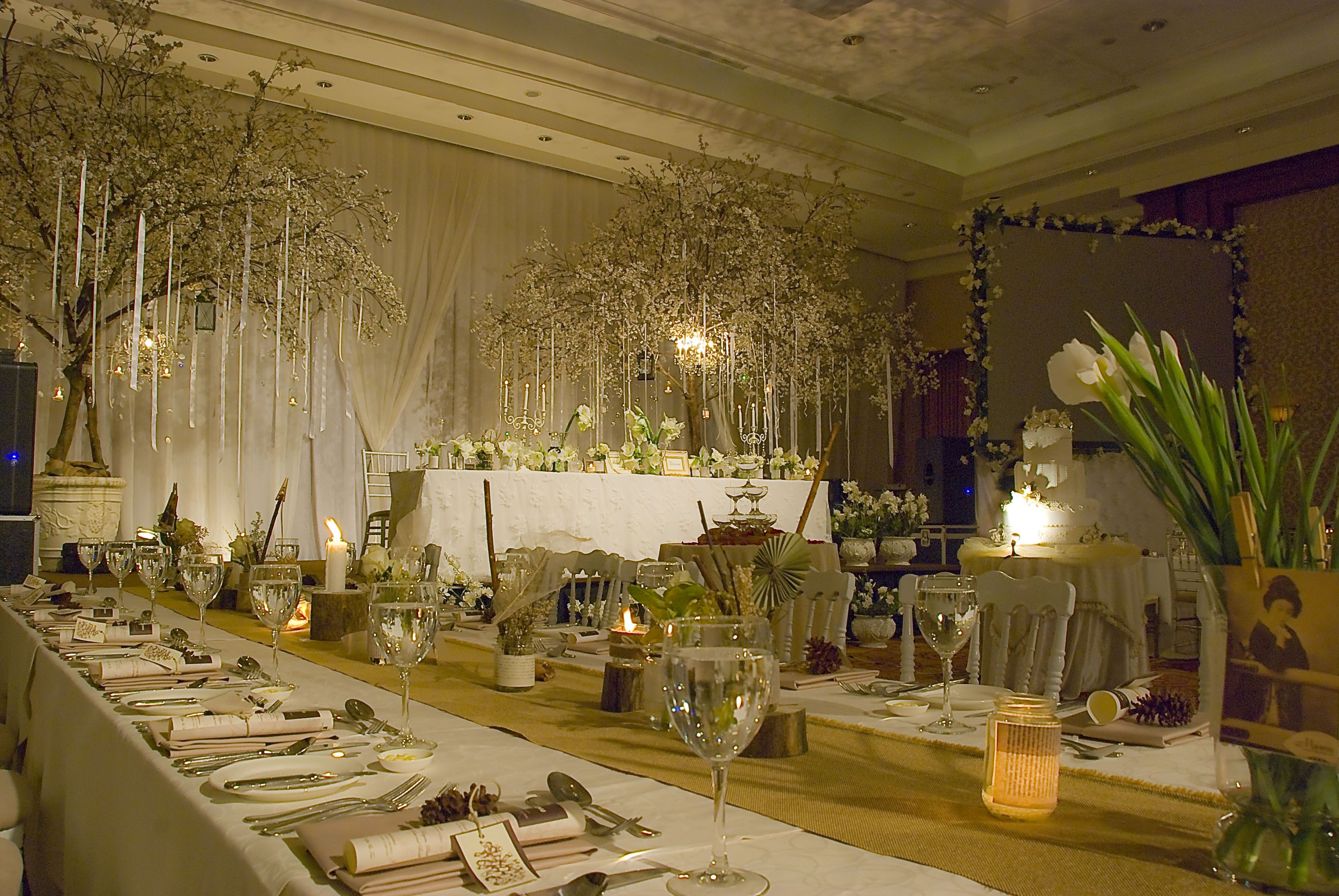 A long banquet table set for a formal event, with candles, glassware, and floral decorations.