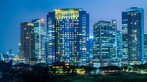 Un paisaje urbano al atardecer con edificios altos iluminados, incluyendo un hotel destacado con una sección superior distintiva.