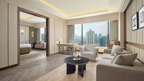 Habitación de hotel moderna con un ventanal grande que ofrece vistas a la ciudad, una zona de estar acogedora, un escritorio y una habitación separada.