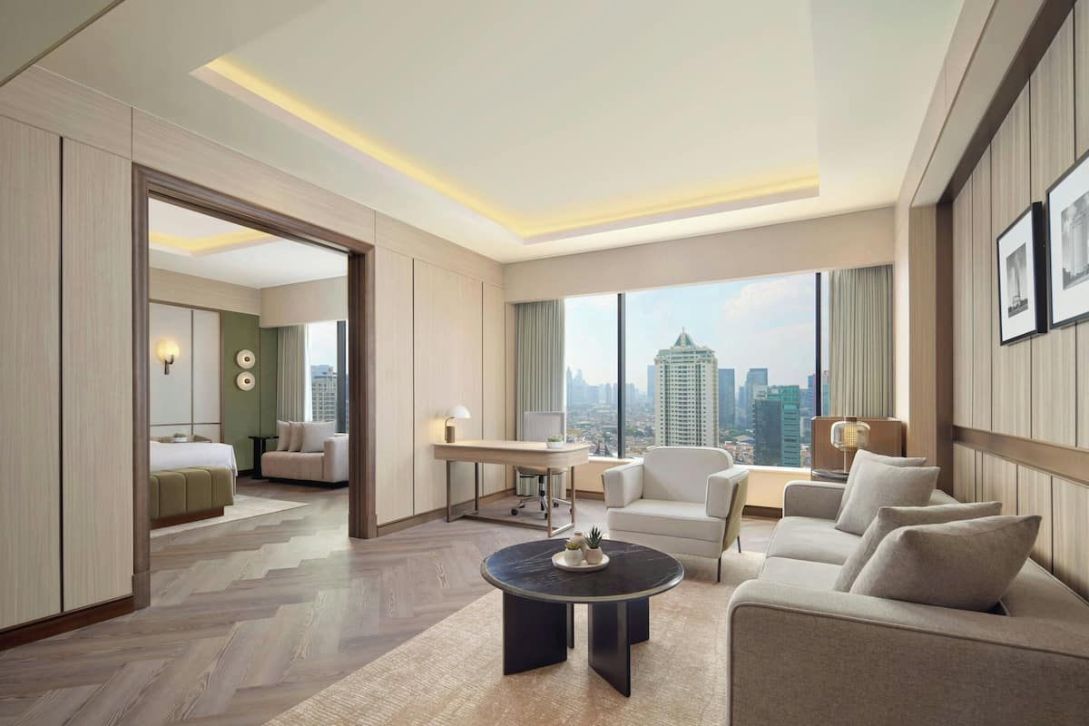 Ein modernes Hotelzimmer mit großem Fenster und Blick auf die Stadt, einer gemütlichen Sitzecke, einem Schreibtisch und einem separaten Schlafbereich.