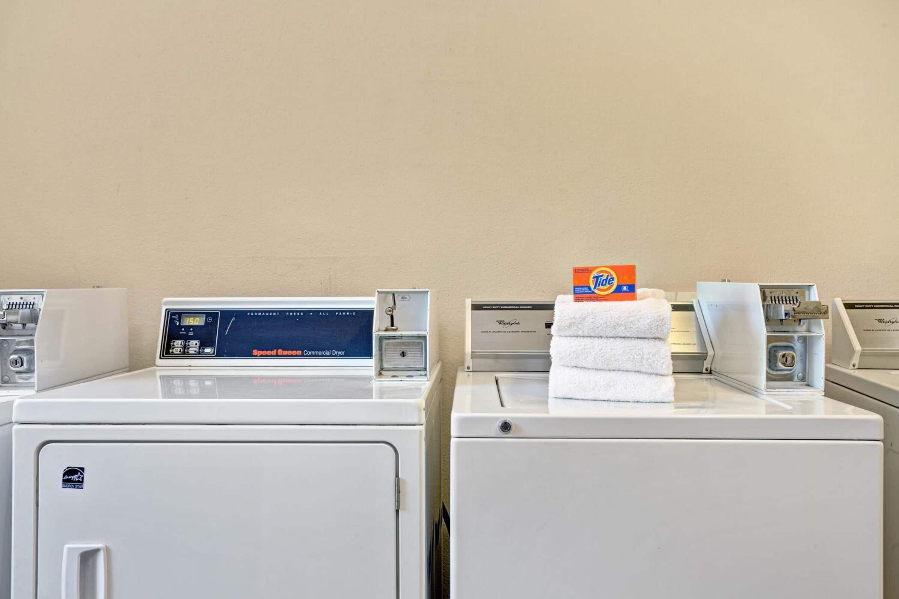 A laundry area with two front-loading washing machines and a Speed Queen Commercial Dryer.