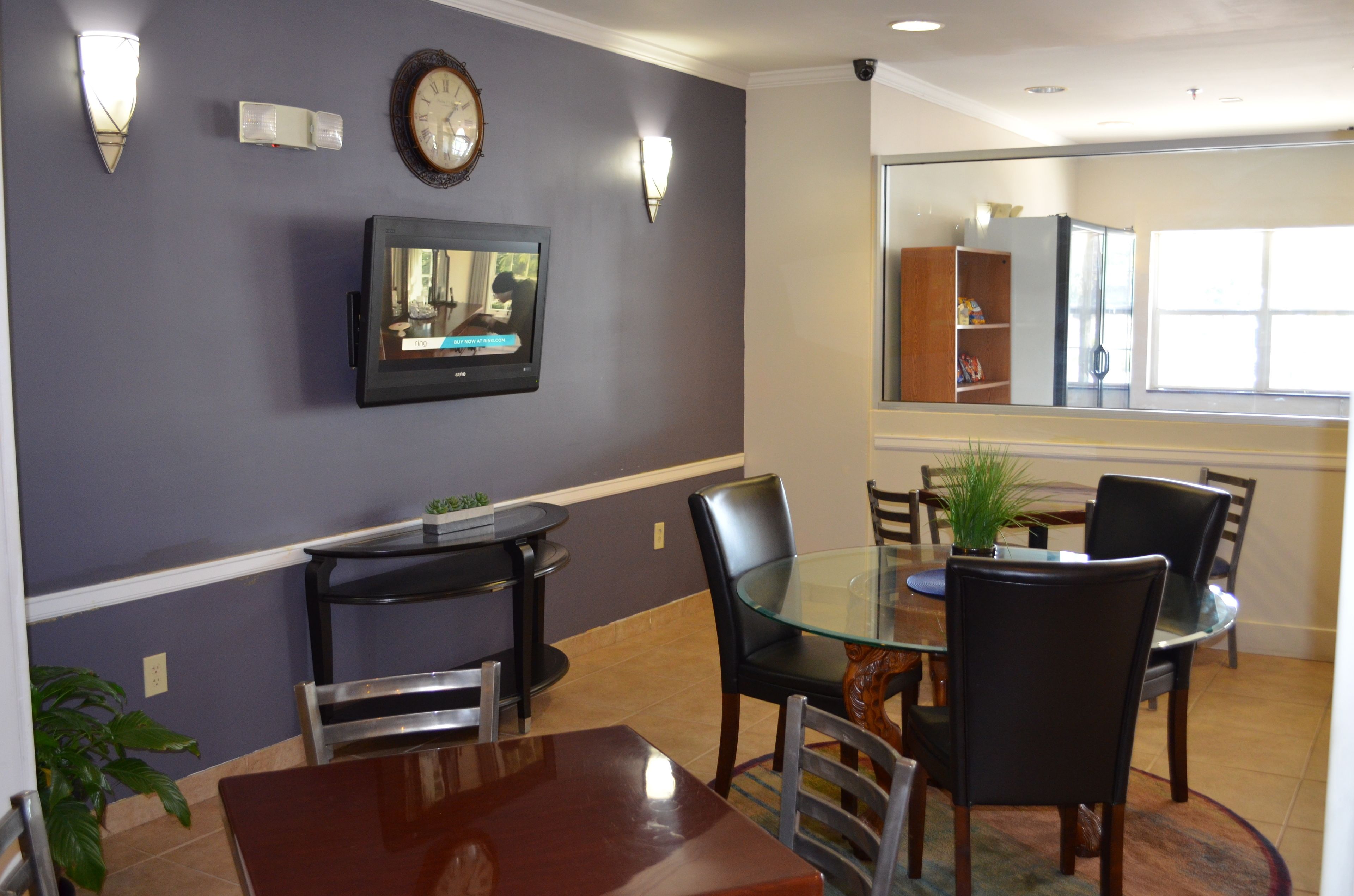 Un comedor con mesa de vidrio, sillas y televisor montado en la pared.