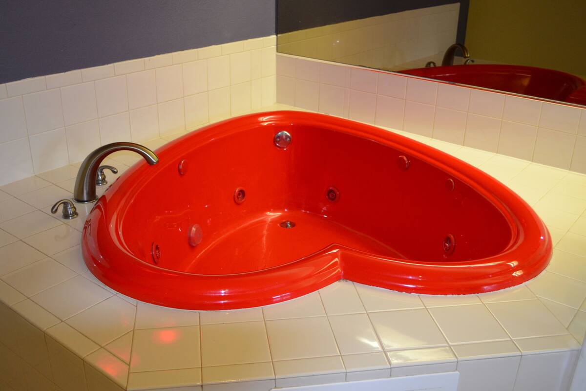 A red bathtub in a bathroom with white tiles.