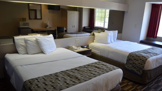 A hotel room with two beds, a desk, a mirror, a window with red curtains, and a microwave. - Stay Express Inn & Suites Atlanta (Union City)