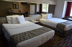 Ein Hotelzimmer mit zwei Betten, einem Schreibtisch, einem Spiegel, einem Fenster mit roten Vorhängen und einer Mikrowelle.