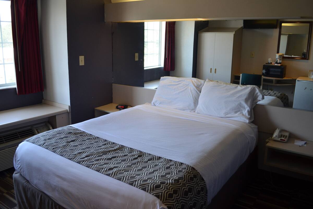 A hotel room with a large bed, a desk, a chair, a mirror, and a window with curtains.